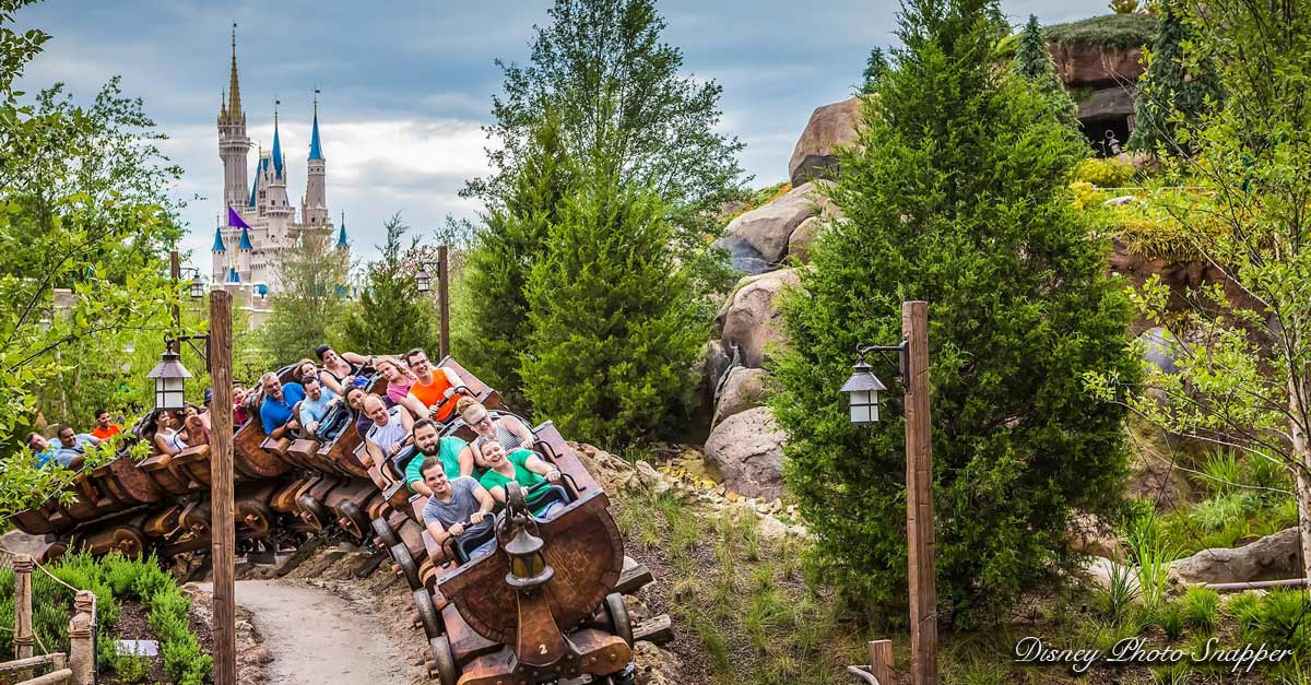 Guests speed through Fantasyland on the Seven Dwarfs Mine Train, with Cinderella Castle and lush trees completing the magical scene.