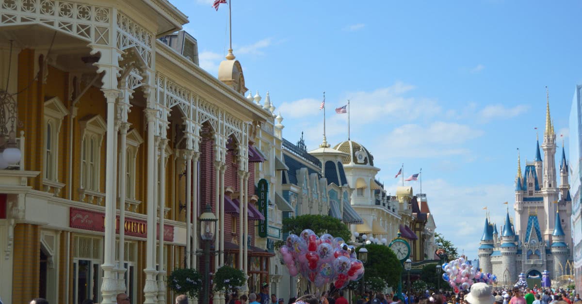 Guests fill Main Street USA, heading toward Cinderella Castle at Disney World under clear skies, surrounded by colorful balloons.