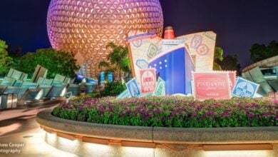 Spaceship Earth lights up Epcot at night with vibrant festival flowers and a Food & Wine Festival sign welcoming guests.