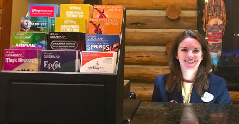 A friendly Disney Cast Member greets guests behind a desk with official park maps and brochures neatly arranged on display.