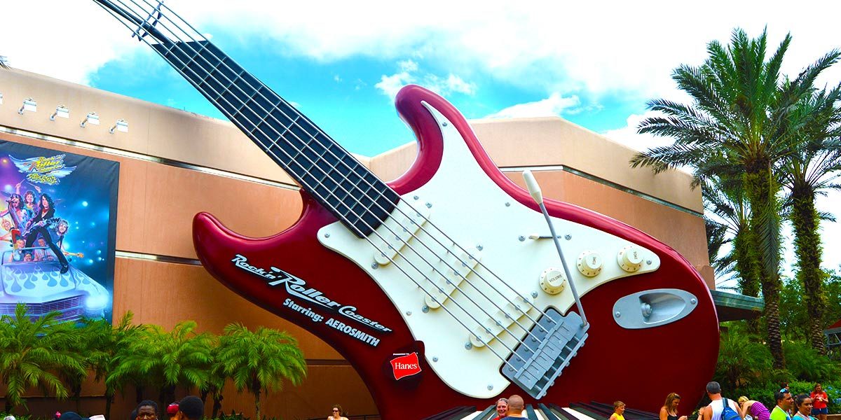 The iconic red guitar greets guests outside Rock 'n' Roller Coaster at Hollywood Studios, surrounded by palm trees and visitors.
