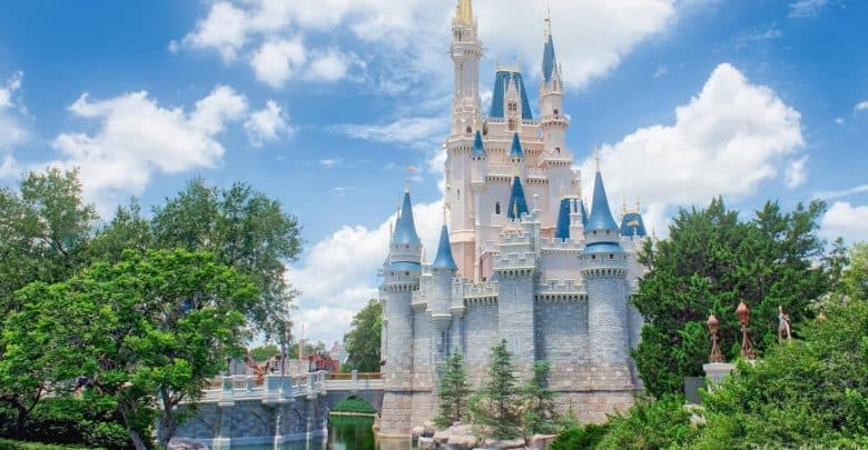 Sleeping Beauty Castle with its iconic blue spires rises above lush trees beneath a bright, partly cloudy sky at Disneyland.