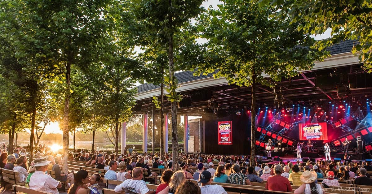 Guests at Universal Studios enjoy a sunset concert, relaxing on benches as a band plays on a vibrant, themed stage.