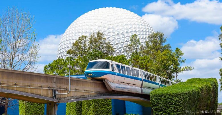 A Disney monorail glides past Spaceship Earth at Epcot, set against a bright blue sky dotted with fluffy clouds.