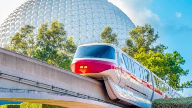 The Walt Disney World monorail glides past Epcot’s iconic Spaceship Earth under a bright Florida sky, framed by lush greenery.