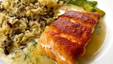A colorful entree of grilled salmon topped with sauce, wild rice, and asparagus served at Epcot’s World Showcase restaurant.