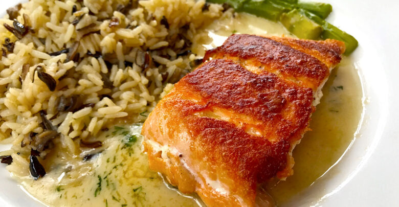 A colorful entree of grilled salmon topped with sauce, wild rice, and asparagus served at Epcot’s World Showcase restaurant.