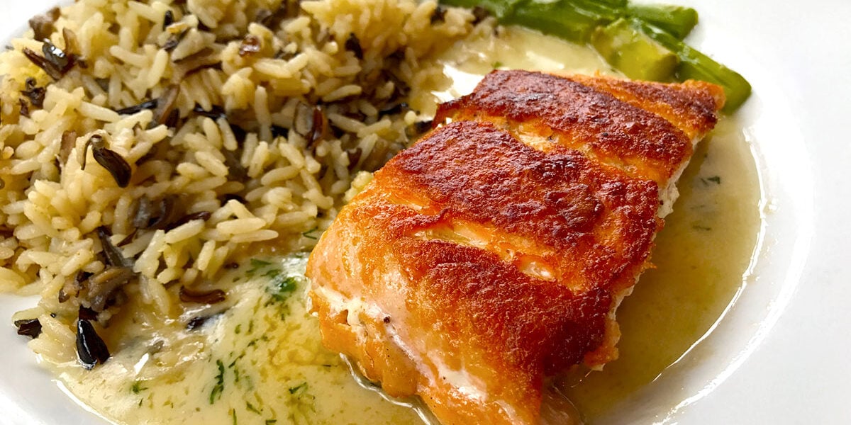 A colorful entree of grilled salmon topped with sauce, wild rice, and asparagus served at Epcot’s World Showcase restaurant.