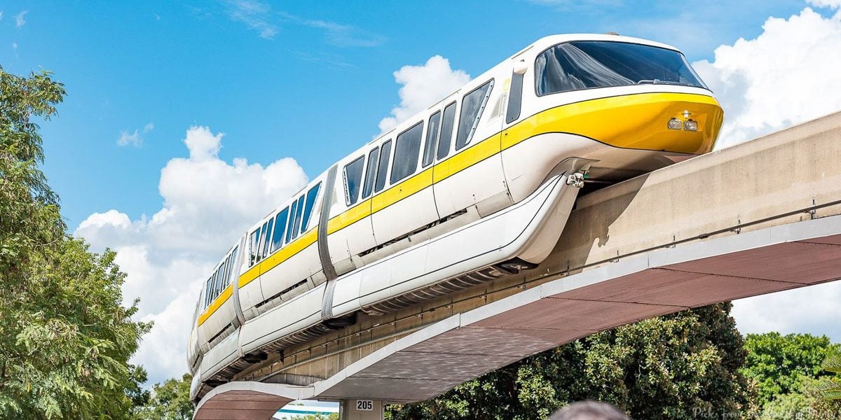 The iconic yellow and white Disney monorail glides above lush trees, set against a bright blue sky at Walt Disney World.