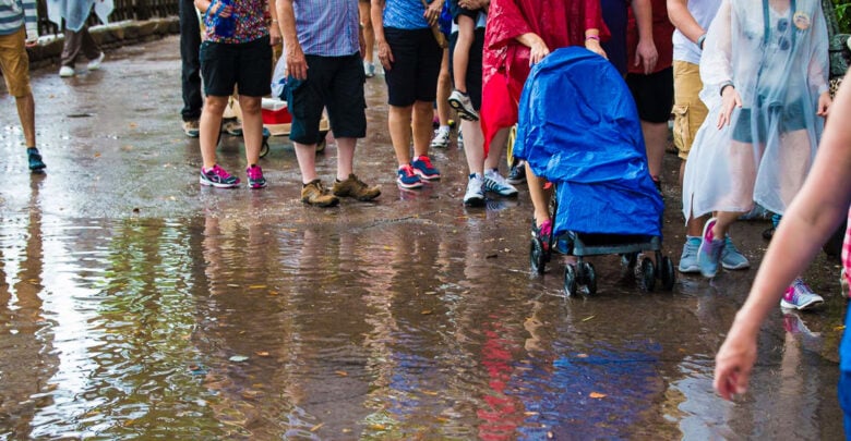 Guests wade through a puddle at Disneyland, their stroller protected by a blue rain cover—proof that smart packing keeps families dry.