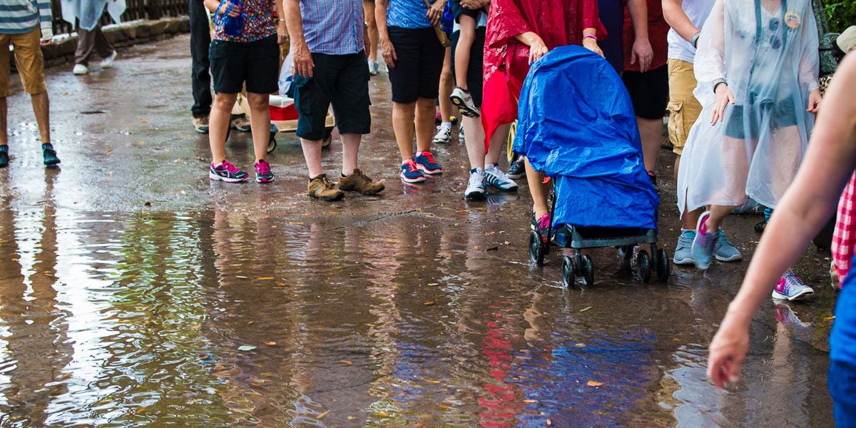 Guests wade through a puddle at Disneyland, their stroller protected by a blue rain cover—proof that smart packing keeps families dry.