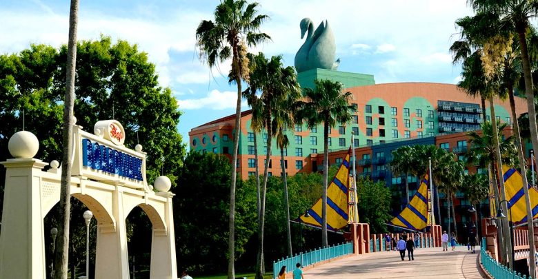 Ornate entry arch and bridge welcoming guests to the vibrant Walt Disney World Swan Hotel, framed by palms and a sunny sky.