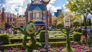 Disney character topiaries in a vibrant EPCOT garden, with the France Pavilion’s clock and Parisian building in the background.