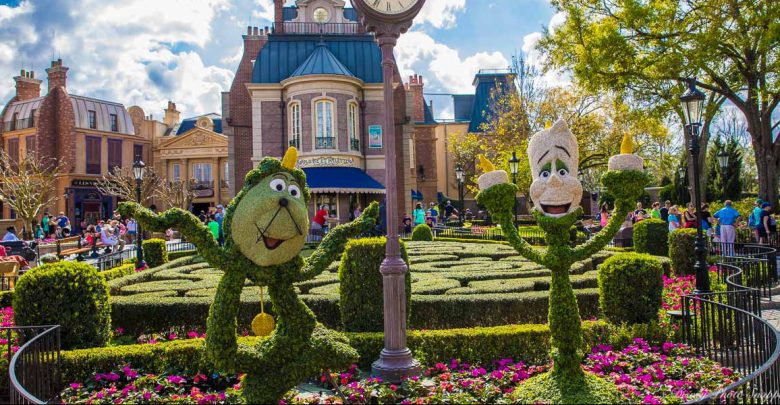 Disney character topiaries in a vibrant EPCOT garden, with the France Pavilion’s clock and Parisian building in the background.