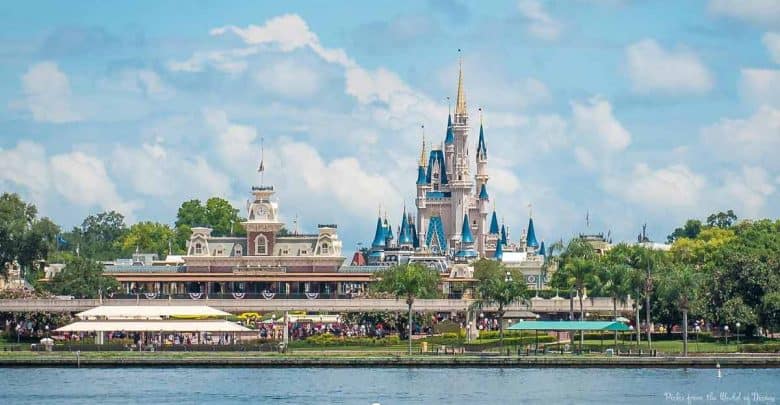 Cinderella Castle towers over Main Street at Disney World, framed by a shimmering lake and lush trees on a bright blue-sky day.