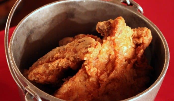 Crispy fried chicken served in a themed metal bucket atop a carnival-red table, perfect for refueling at an amusement park eatery.