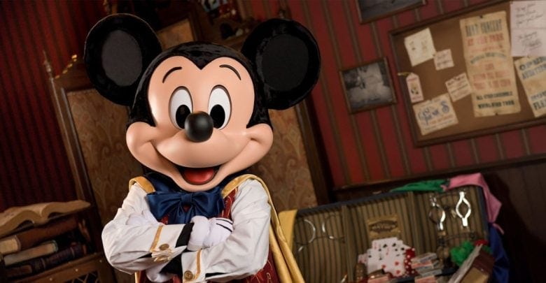 Mickey Mouse stands smiling with arms crossed in a cozy, vintage room filled with books, posters, and playing cards. Warm lighting and whimsical decor evoke the enchanting charm of classic Magic Kingdom Experiences.