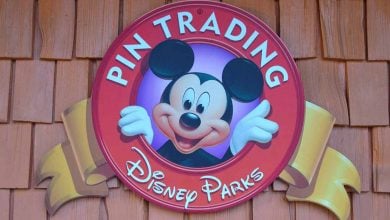 Disney Parks Pin Trading sign featuring Mickey Mouse, displayed on a wooden shingle wall inside the park.