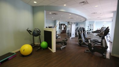 A vibrant fitness zone with rows of cardio gear, bright exercise balls, and mats on sleek wood floors beneath playful blue walls.