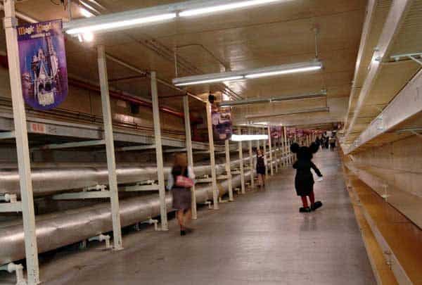 Mickey Mouse strolls through a quiet, banner-lined tunnel with shelves, creating backstage magic at Disney World.