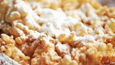 Golden funnel cake covered in powdered sugar, ready to enjoy on the midway at your favorite theme park.