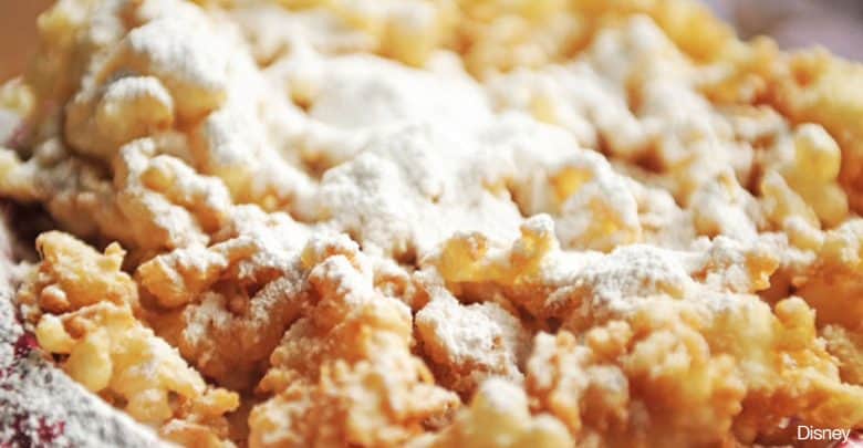 Golden funnel cake covered in powdered sugar, ready to enjoy on the midway at your favorite theme park.