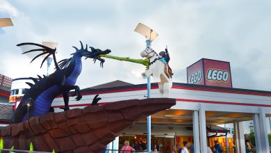A Lego dragon faces off with a Lego knight on horseback outside the entrance to LEGOLAND, beneath dramatic cloudy skies.