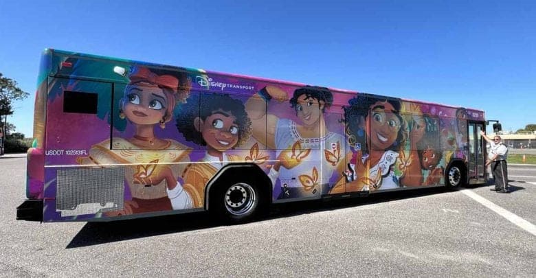 A city bus wrapped with colorful artwork featuring Disney’s "Encanto" characters, including Mirabel, butterflies, and vibrant patterns—a magical showcase of How to Get Around Disney World. A person stands near the front of the bus.