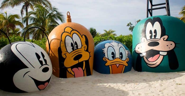 Giant beach buoys featuring Mickey, Pluto, Donald, and Goofy faces brighten a palm-lined shoreline at Disney’s Castaway Cay.
