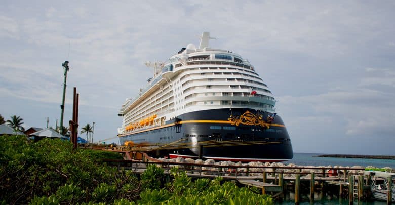 A cruise liner awaits guests at the Disney Cruise Line port, lush landscapes and shimmering blue sea setting the scene.