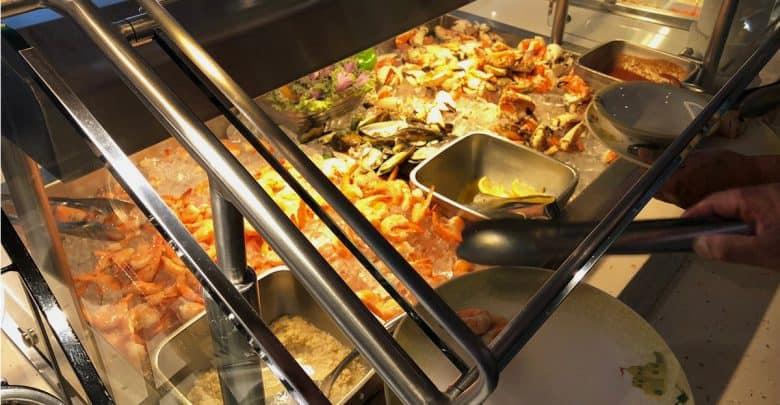 Seafood buffet station at the theme park, featuring shrimp, crab legs, lemon wedges, and sauces behind glass for guests.