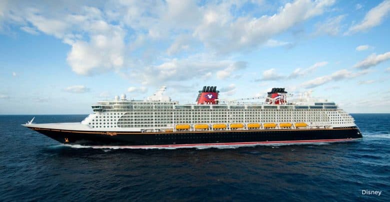 Disney Cruise Line ship with iconic red funnels and yellow lifeboats sailing at sea beneath a partly cloudy sky.