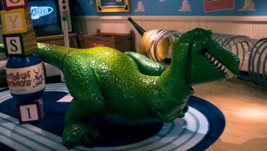 Rex from Toy Story on a bright blue rug with colorful blocks, set against a playful Toy Story Land backdrop.
