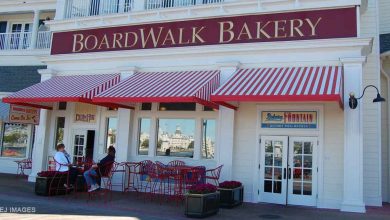 Guests relax at red tables outside Disney’s BoardWalk Bakery, shaded by classic red-and-white striped awnings.