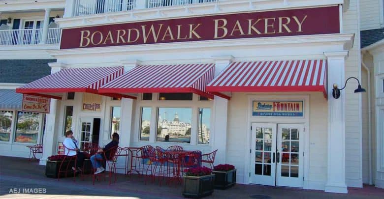 Guests relax at red tables outside Disney’s BoardWalk Bakery, shaded by classic red-and-white striped awnings.