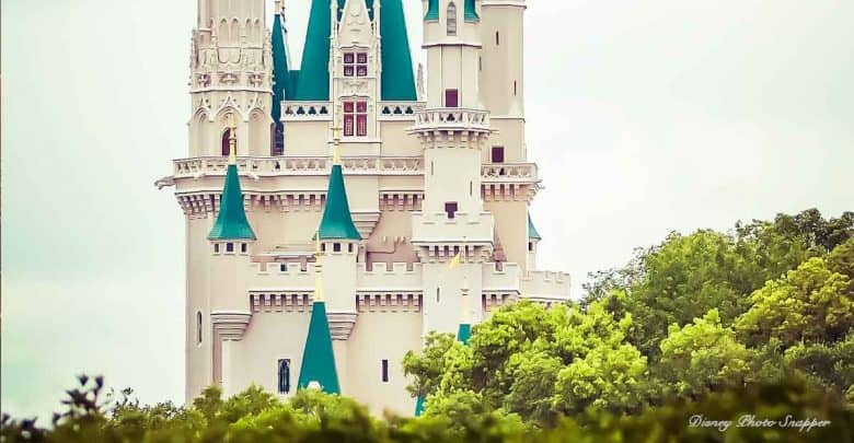 The iconic teal-spired castle towers over lush greenery at Disneyland, set against a dramatic cloudy sky.