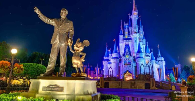 Walt Disney and Mickey Mouse pose together in front of the glowing Cinderella Castle at night in Walt Disney World.