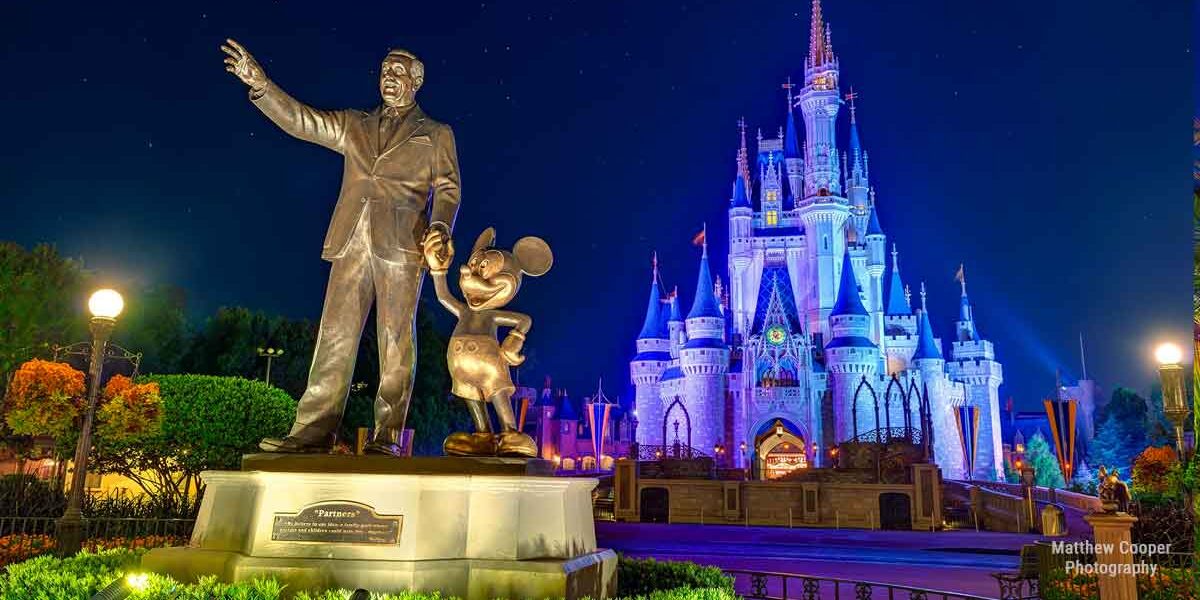 Walt Disney and Mickey Mouse pose together in front of the glowing Cinderella Castle at night in Walt Disney World.