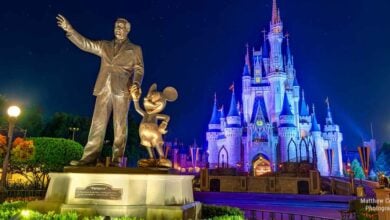 Walt Disney and Mickey Mouse statue shining in front of Cinderella Castle, spectacularly lit up at night in Magic Kingdom.