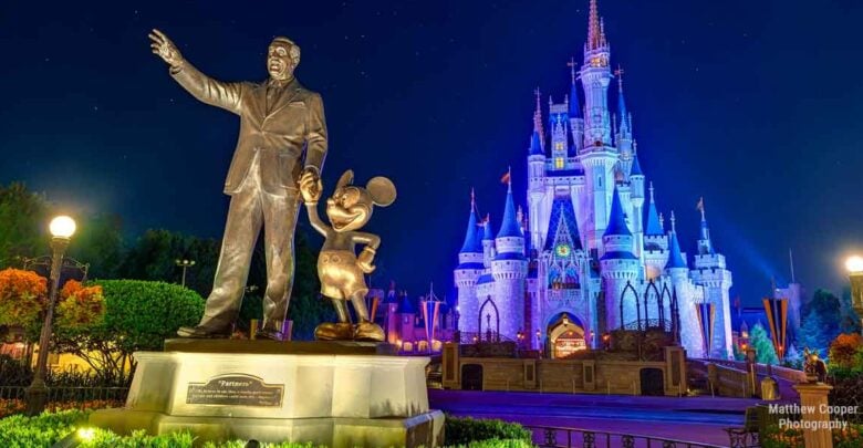 Walt Disney and Mickey Mouse statue shining in front of Cinderella Castle, spectacularly lit up at night in Magic Kingdom.