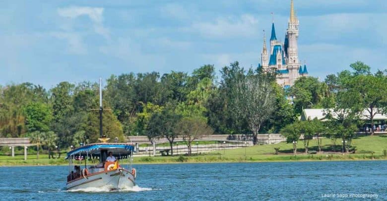 A boat glides across a lake with a Disney castle and lush trees under a clear blue sky, evoking iconic park magic.