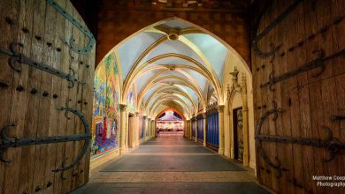 Grand wooden doors swing open to a vibrant, vaulted hallway like entering a magical Disney castle, warmly illuminated ahead.