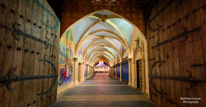 Grand wooden doors swing open to a vibrant, vaulted hallway like entering a magical Disney castle, warmly illuminated ahead.
