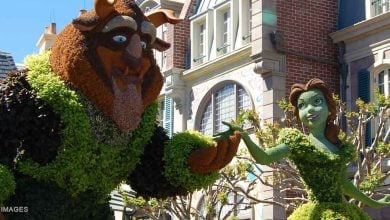 Beast and Belle topiary statues welcome guests at EPCOT, set against charming European-inspired park architecture.
