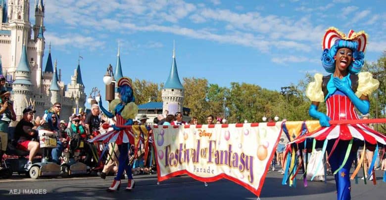 Festival of Fantasy Parade performers lead with the signature banner at Magic Kingdom, signaling a can't-miss Disney celebration.