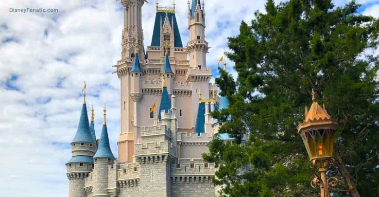 Cinderella Castle’s blue spires rise above Main Street, flanked by lush trees and a themed lamp beneath Disney’s bright skies.