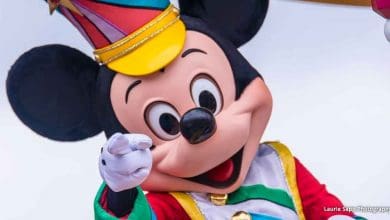 Mickey Mouse at Disney World, wearing a vibrant costume and hat, smiles and points cheerfully at guests for a fun photo op.