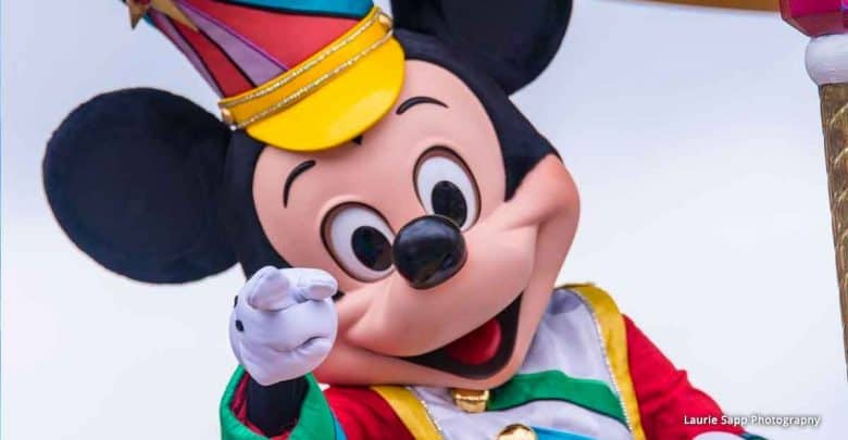 Mickey Mouse at Disney World, wearing a vibrant costume and hat, smiles and points cheerfully at guests for a fun photo op.