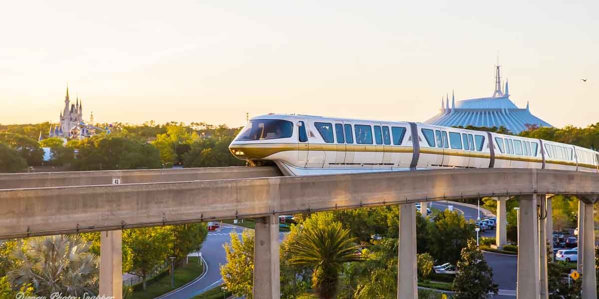 The iconic Disney Monorail glides past lush trees, with Cinderella Castle and Space Mountain lit by the golden sunset at Magic Kingdom.