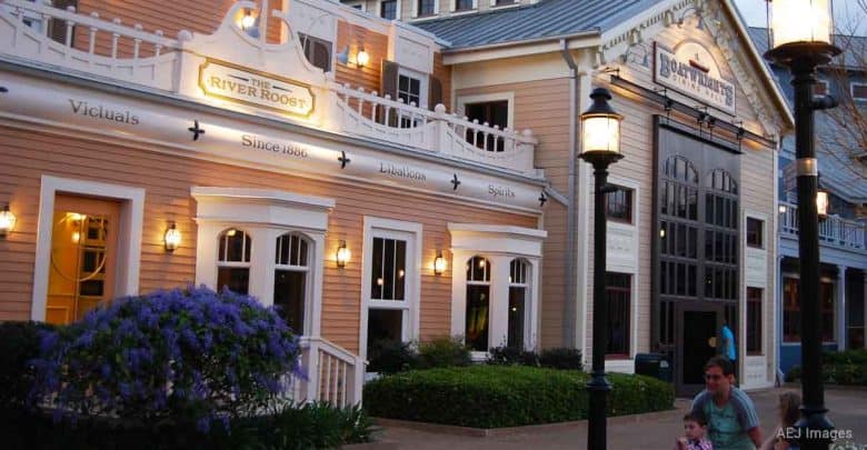 Charming Main Street facade with white trim, nostalgic signs, and street lamps, as guests stroll through the park entrance.